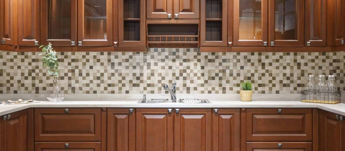 Contemporary upscale home kitchen interior with wood cabinets and floors, granite countertop, accent lighting and stainless steel appliances