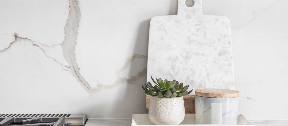 A beautiful closeup of a custom designed kitchen, with marble looking quartz countertop and backsplash. Decorated by marble cheese board and little indoor planter.