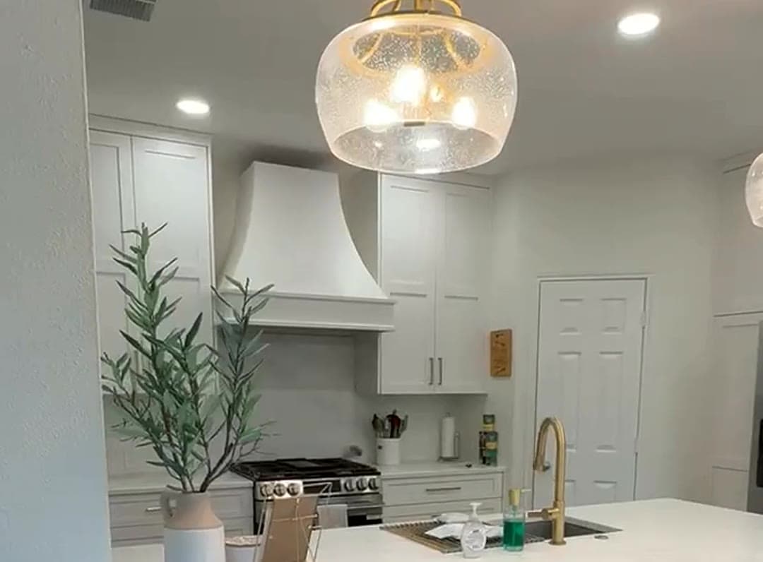 Custom white kitchen with glass pendant light, plaster range hood, brass faucet and quartz island by LuxeCraft in San Antonio
