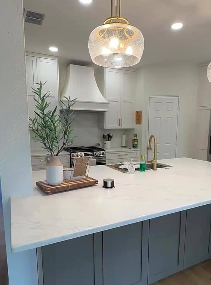 Custom white kitchen with seeded-glass pendant, range hood, brass faucet and quartz island by LuxeCraft in San Antonio