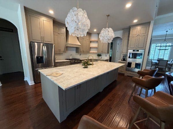 Open kitchen with glass pendant lights over a large quartzite island and custom cabinets by LuxeCraft